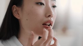 Lips care. Close up portrait of young pretty asian lady applying pampering balm on lips with finger at home, looking aside, slow motion, empty space - Powered by Shutterstock - Get 15% off with code: PIKWIZARD15