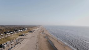Drone flies over ocean beach outside the city on a summer day. Calm light blue ocean with small waves. Arial view of ocean shore with beach houses on a sunny day. High quality 4k footage
