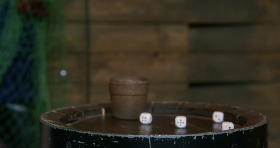Person puts a large ceramic mug with an emblem on a small round wooden table, where the cup and dice are scattered, close up. An underground gambling bar Royalty-Free Stock Footage #1091036083