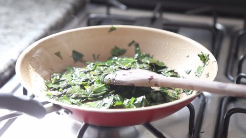 Female hands cooking ora-pro-nobis in frying pan. Stirring wooden spoon. Pereskia aculeata is a popular vegetable in parts of Brazil
