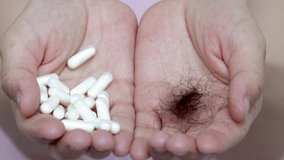 hair loss problem and treatment concept.young woman with a white pills, capsules, in one hand and a ball of fallen hair in another. lack of vitamins, minerals.4k close up video of hands