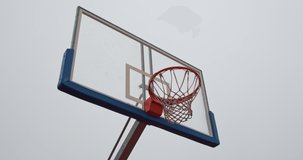 Low angle view of a basket on an empty basketball court on a cloudy spring morning against the cloudy grey sky.