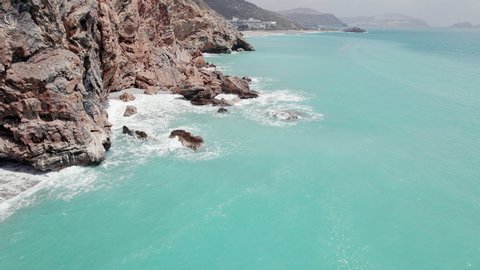 Aerial view of sheer cliff and splashing waves of turquoise colored sea