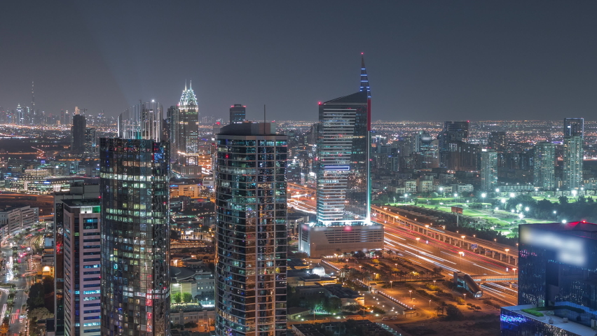 Aerial view of media city and al barsha heights district area night timelapse from Dubai marina. Towers and illuminated skyscrapers with traffic on a highway from above