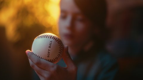 Close Up Portrait of a Young Sports Fan Holding a White Baseball Ball at Home. Excited Boy Looking at the Ball and Turning It Round. Enjoying Leisure Time in Nostalgic Retro Childhood Concept.