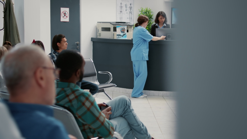 Busy hospital reception lobby with diverse patients to attend checkup visit, using appointment report to help people with disease. Waiting room area for healthcare consultation and examination. | Shutterstock HD Video #1091046901