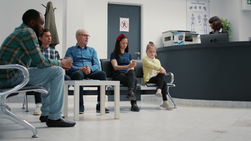 Many patients sitting in waiting area lobby at hospital reception, preparing to start checkup visit with appointment. Mother with child, senior man and other people in waiting room. Tripod shot. Royalty-Free Stock Footage #1091046917