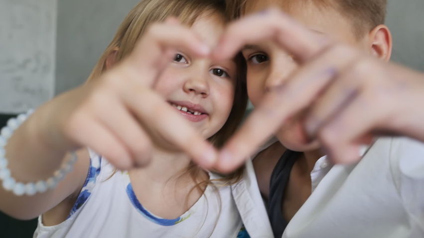 Two girls of European appearance, stretching out their hands, made a heart with their fingers, connecting them together and looking into the heart. slow motion