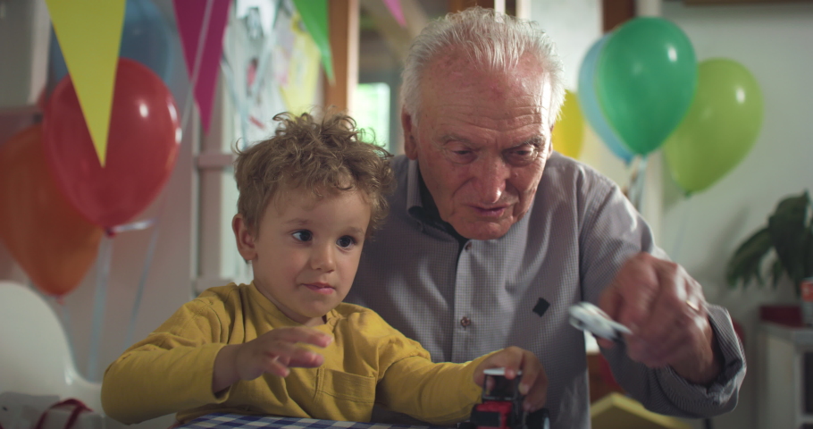 Cinematic shot of happy senior grandfather is playing with aircraft and tractor toys with his grandson toddler boy while enjoying to pass time together during birthday celebration with family at home. Royalty-Free Stock Footage #1091050131