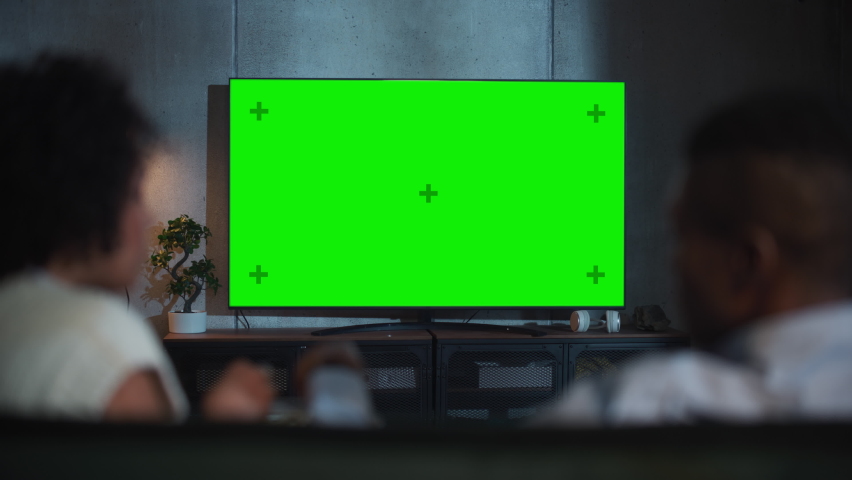 Back View of the Black Couple Eat Popcorn on the Sofa and Watching TV with Green Screen Mock Up Display at Loft Room. Rack Out of Focus Couple Close Up Shot at Night Royalty-Free Stock Footage #1091050377