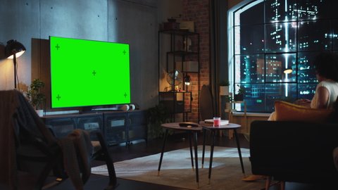 Moving Camera Shot of Black Boyfriend and Girlfriend Sitting on a Sofa in Living Room, Eating Popcorn and Watching TV with Green Screen Display. Couple Embracing and Have Pleasant Evening