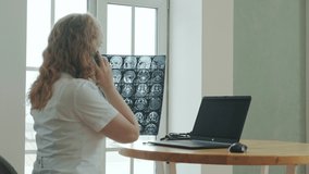 Adult Caucasian Female doctor works in clinic at computer. specialist examines X-ray and talks to patient on phone. concept of online healthcare. Medical Care Virtual consultation