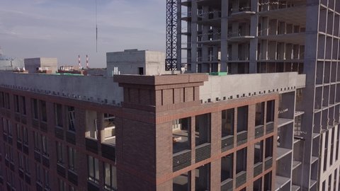 Unfinished building with huge undefined windows and materials on roof by highrise construction under blue sky aerial view