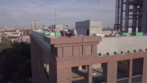 Unfinished building corner with huge undefined windows on walls and construction materials equipment on roof aerial view