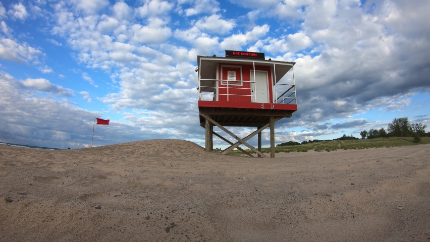 Timelapse footage of lifeguard tower on sandy lakefront beach on warm summer day day with blue sky and clouds