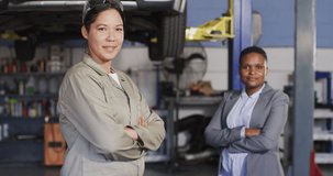 Video of two diverse happy female car mechanic and business owner looking at camera. working in car repair shop and running small feminine business concept.