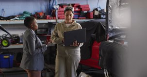Video of two diverse car mechanic and business owner with laptop searching for car parts. working in car repair shop and running small feminine business concept.