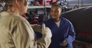 Video of two diverse female car mechanics talking in workshop. working in car repair shop and running small feminine business concept.