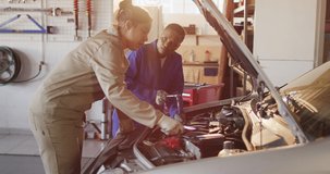 Video of two diverse female car mechanics talking and repairing car. working in car repair shop and running small feminine business concept.