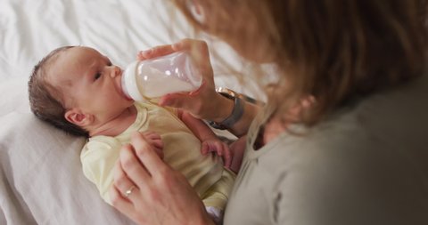 Video of happy caucasian mother feeding newborn baby with bottle on bed. motherhood, parental love and taking care of newborn baby concept digitally generated video.