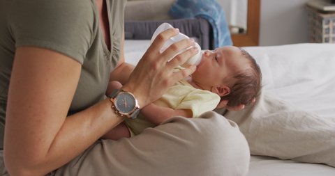 Video of midsection of caucasian mother feeding newborn baby with bottle on bed. motherhood, parental love and taking care of newborn baby concept digitally generated video.