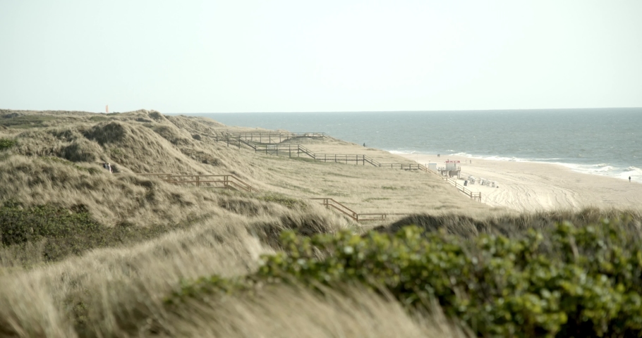 Wooden piers trough the dunes of Sylt with the beach and the Northsea in the background 4k 60fps