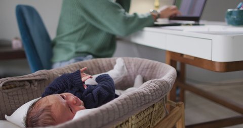 Video of caucasian mother working on laptop from home with newborn baby. motherhood, parental love and taking care of newborn baby concept digitally generated video.