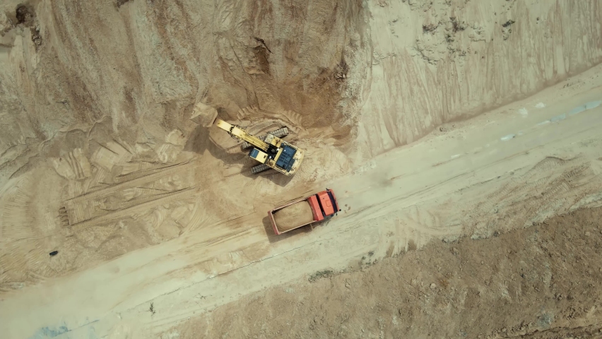 Aerial top down view of an excavator loading sand into a dump truck in sand quarry