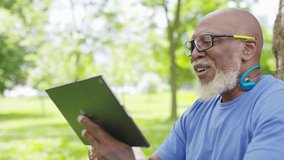 Senior black male having a video call on a digital tablet outdoors in the park
