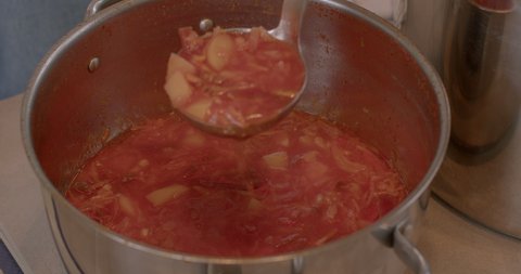 Large pots of borscht is soup variant of Ukrainian origin, made with red beetroots as one of the main ingredients, which give the dish its distinctive red color. Closeup. Ladle is huge kitchen spoon.