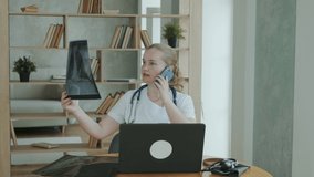 Professional doctor works at clinic. female therapist in overalls with stethoscope around her neck carefully examines the MRI of patient's head and consults with colleagues by phone