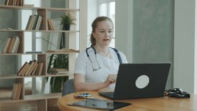 Professional doctor works at clinic. female therapist in overalls with stethoscope communicates via videoconference with patient and explains how to take prescription pills. Medical Care Online