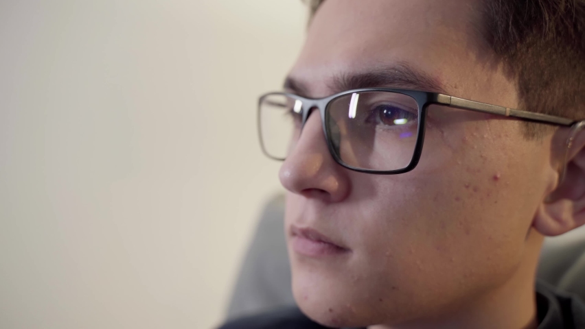 The guy with glasses is watching TV. Close-up of a focused young man. The guy wears computer glasses to reduce the strain on his eyes. Royalty-Free Stock Footage #1091078251