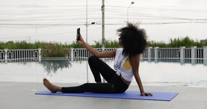 A female dressed for exercise sits on a yoga mat talking smart phone video call.