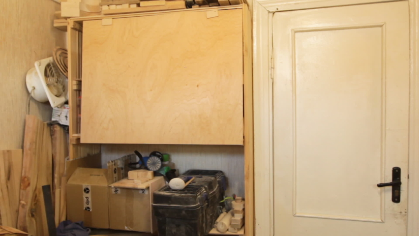 A male carpenter takes out a wooden billet from a cabinet in the workshop for work