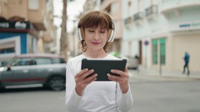 Middle age woman smiling confident watching video by touchpad at street