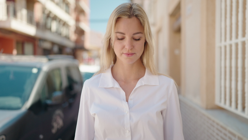 Young blonde woman with relaxed expression standing at street