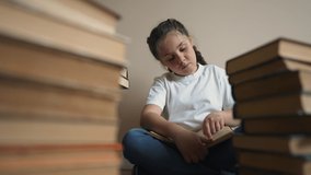 Child sits on floor of library and reads book. Smart generation reads books. teenage girl does her homework on background of bookshelves. School education of child in library. child with book