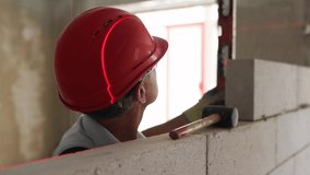 Bricklayer using rubber mallet hammer to tap and level concrete blocks wall. Contractor uses precise spirit bubble and laser level for brickwork. Worker constructs a wall in new apartment real estate. - Powered by Shutterstock - Get 15% off with code: PIKWIZARD15