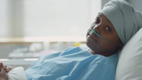 Portrait of sick African American woman with nasal cannula and headwrap lying on bed in hospital ward and posing for camera - Powered by Shutterstock - Get 15% off with code: PIKWIZARD15