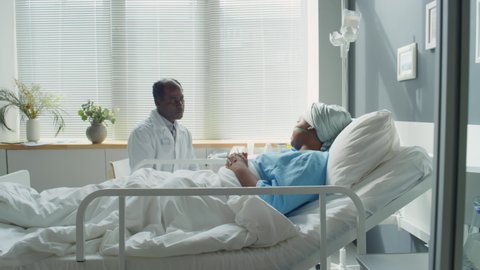 Zoom in shot of careful African American doctor holding hands of young female patient and speaking with her while supporting during therapy in hospital