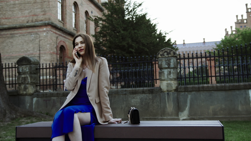 A girl from Ukraine sits in a park in a jacket and speaks on the phone and learns good funny news and laughs