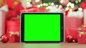 Digital tablet mockup green blank screen for ads on Christmas table holiday background. Xmas shopping online stores e commerce websites, virtual family party Happy New Year video calls concept.