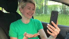 A young woman blogger in a green t-shirt sits in a car, broadcasts live, talks with subscribers, looks at the smartphone screen. Instagram, Social media, video chat and technology concept