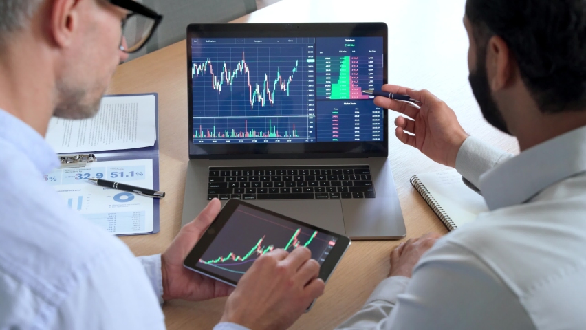 Two diverse traders brokers stock exchange market investors discussing crypto trading charts growth using digital tablet and laptop analyzing financial risks, investment profit, global rates forecast. | Shutterstock HD Video #1091093475