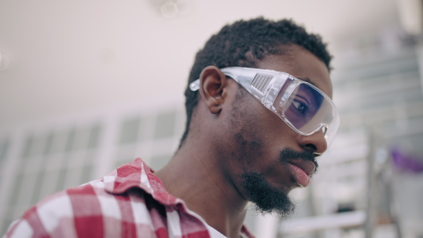 African American man in protective goggles painting wall with paint roller
