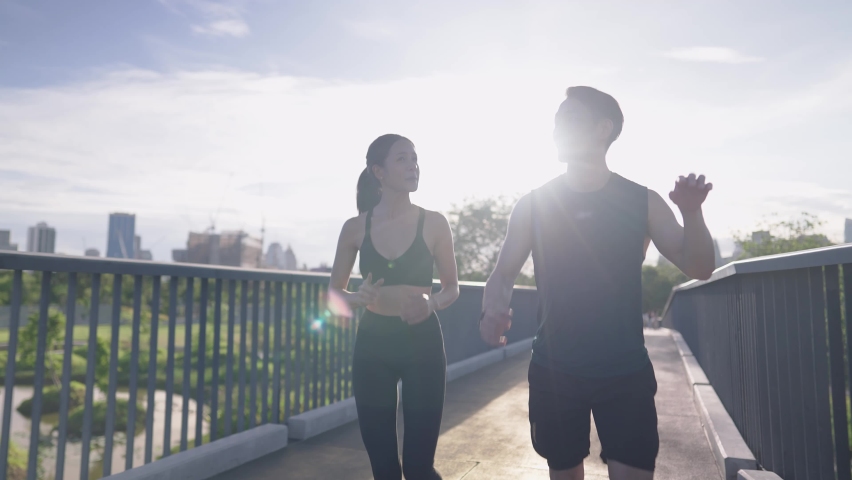 An active asian young couple in sportswear enjoy running jogging outdoors on park walking bridge. Happy athlete people on cheerfully talking while working out. Concept Healthy Motivation and Exercise Royalty-Free Stock Footage #1091097397