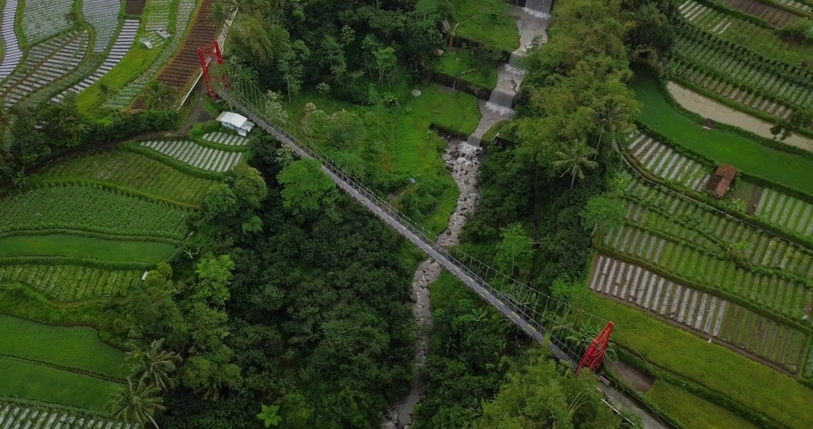 Mangunsuko bridge over river in scenic, tropical valley, rural farmland with fields in Indonesia - aerial drone