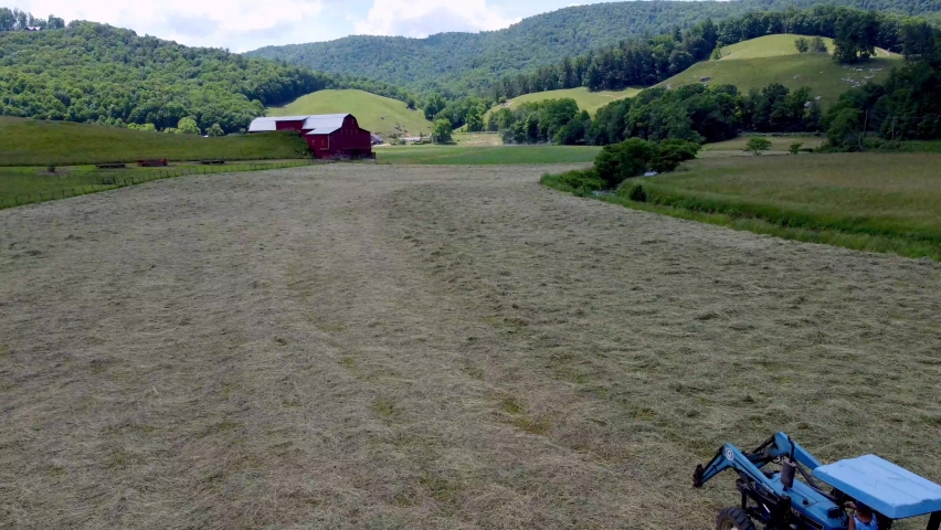 LADY FARMER ON TRACTOR HARVESTING HAY IN SUGAR GROVE NC NEAR BOONE NC, NORTH CAROLINA AERIAL