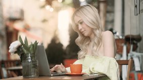 Attractive blond woman sitting in the cafe and talking on laptop by video chat. Girl have a working conversation or talking with friends.